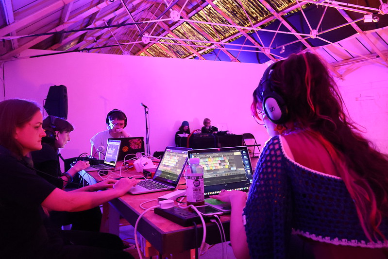 Four people sitting at laptops with sound software open, two sat with electrical equipment in distance