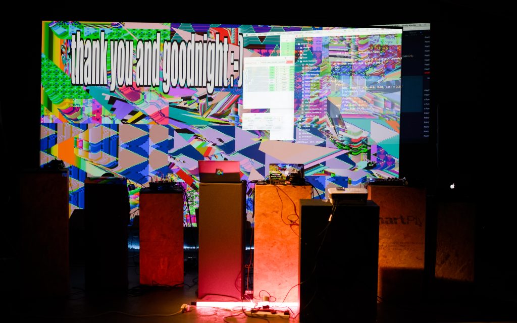 Large projected screen reading "thank you and goodnight :-]" with glitch like shapes colours and patterns