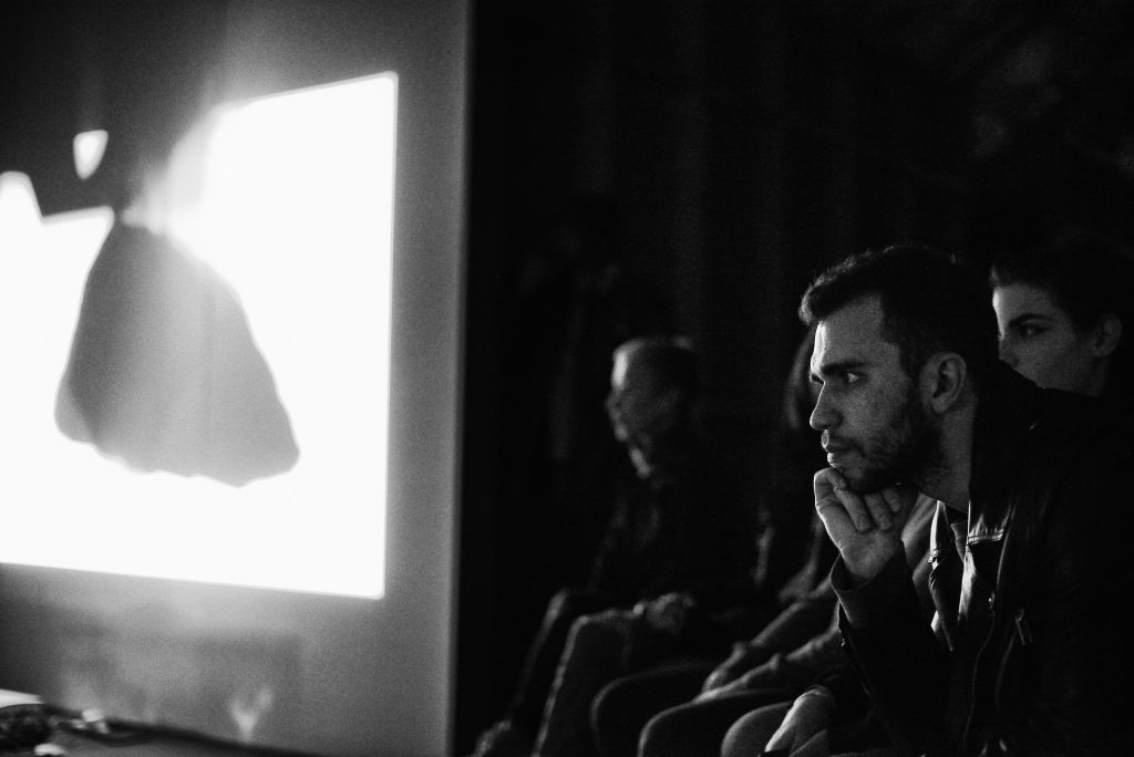 Projected image of silhouetted object on a large screen with audience members looking on