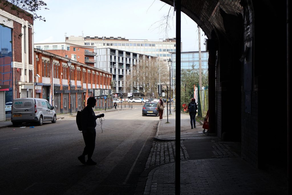 A person in silhouette is making a recording under a railway bridge on an industrial street in central Birmingham near Snow Hill Station