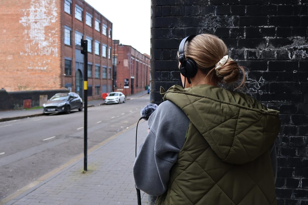 a woman with her back towards us is holding a sound recorder on an industrial street in central Birmingham