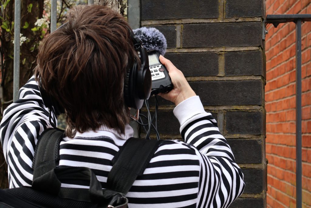 A person with their back towards us is holding a sound recorder by a canal in central Birmingham