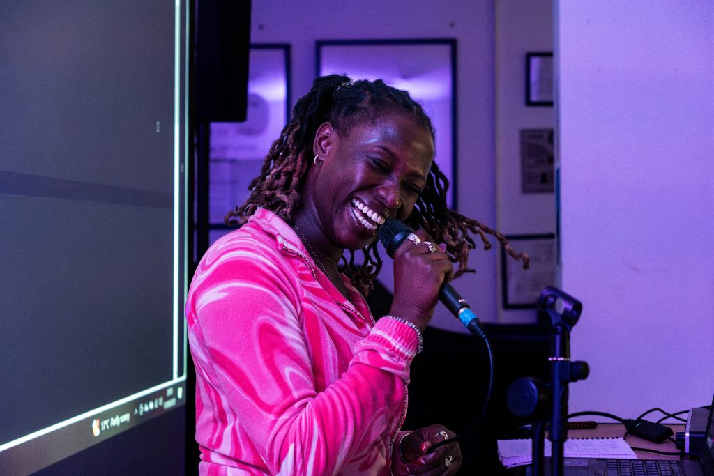 Sheeba Q mid perofmrnce holding the mic and swinging head to the side smiling