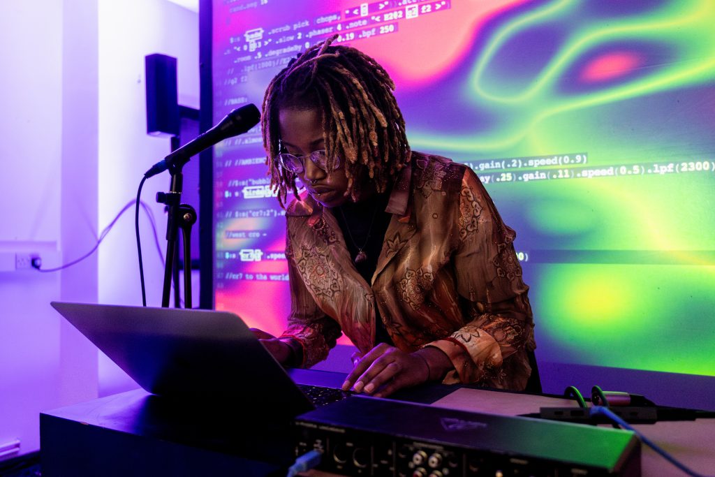 Cyberseed leaning over laptop with colourful screen of code projected in background