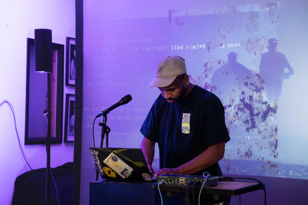David standing at laptop with microphone in front of screen showingcode and silhouettes of two people