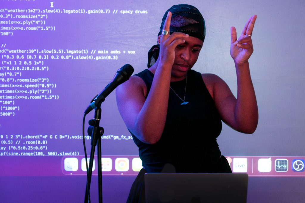okcandice showing 'gun fingers' next to a microphone with code projected in the background
