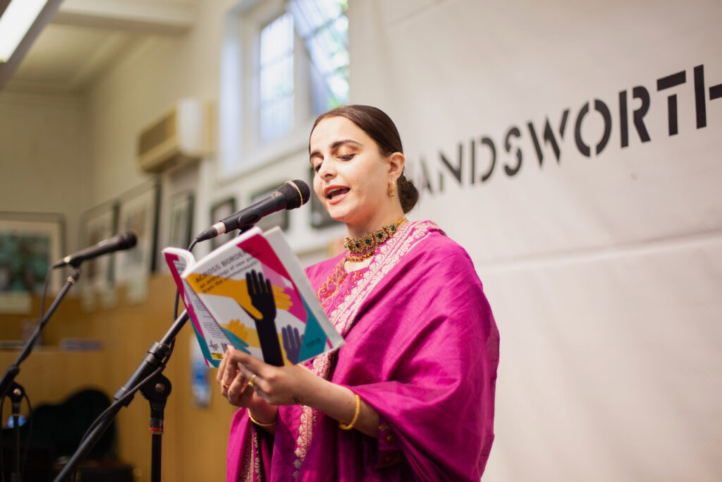 Nafeesa performing, reading from a poetry book into a microphone