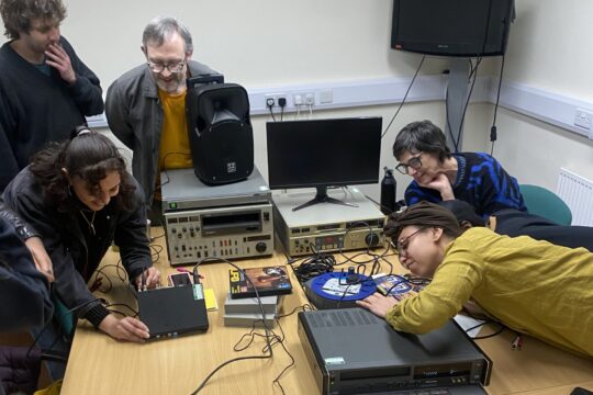 The professional development group working with digitisation equipment, leabing over the table, plugging in wires