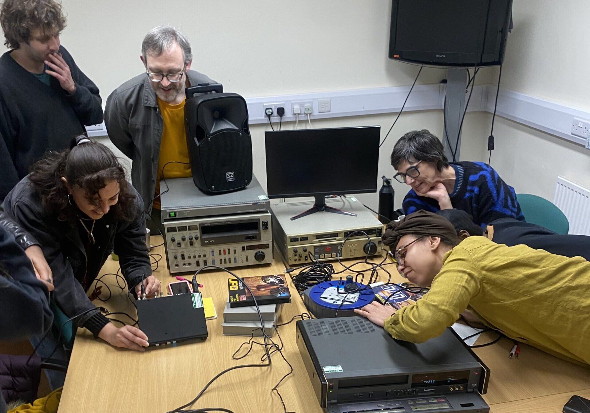 The professional development group working with digitisation equipment, leabing over the table, plugging in wires